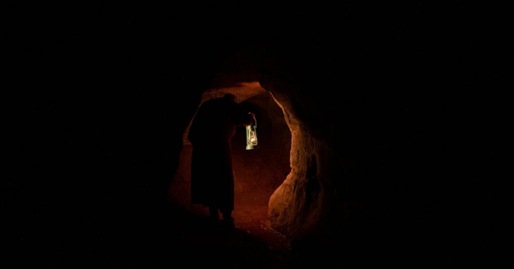 Silhouette of a person holding a lantern in a dark cave, creating a mysterious ambiance.